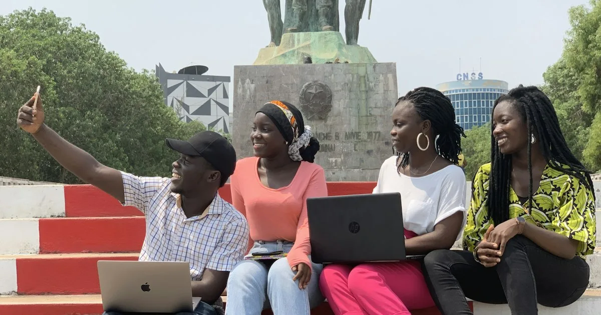 A group of young people sitting together on a bench working on laptops.